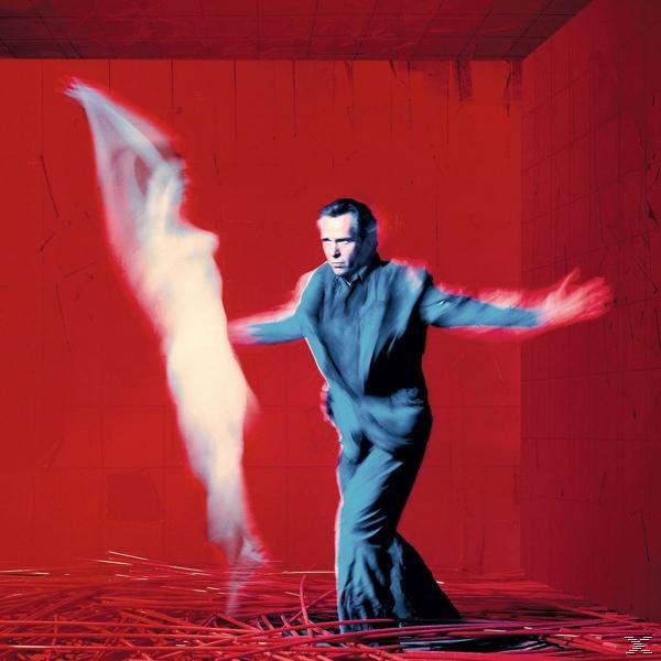 Ein Mann in blauem Anzug tanzt in einem roten Raum, mit einer geisterhaften Figur.