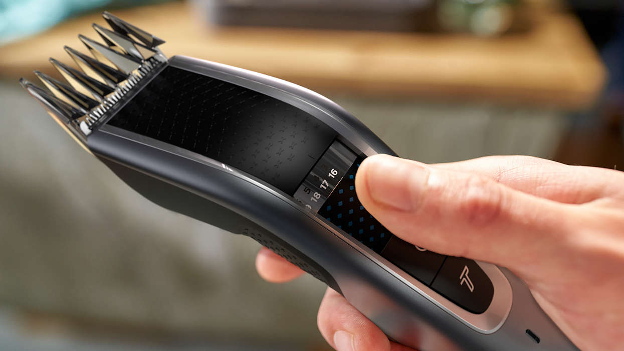 Close-up of a person's hand adjusting a hair clipper's length settings.