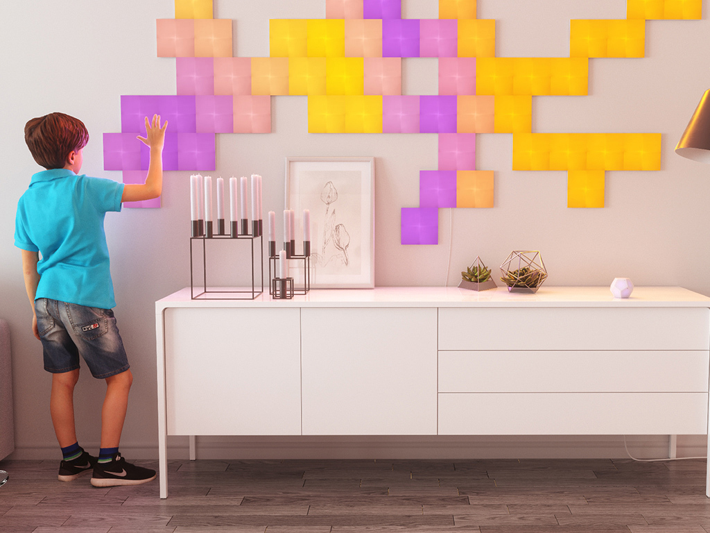 Ein Junge berührt eine Wand mit bunten, beleuchteten Quadraten. Ein weißer Schrank hält Objekte.