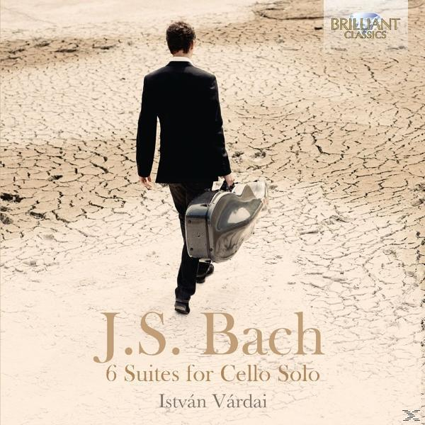 Fekete öltönyös férfi repedezett földön sétál. J.S. Bach, 6 Suites for Cello Solo szöveg alul.