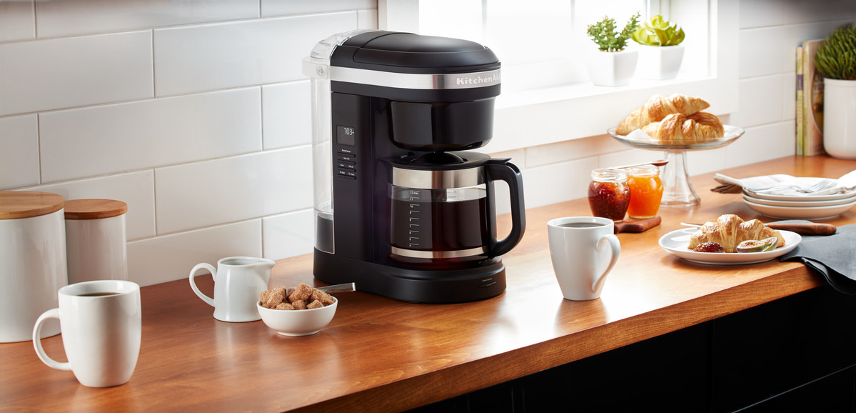 Kaffeemaschine auf Holztisch mit Tassen, Zuckerdose und Gebäck.