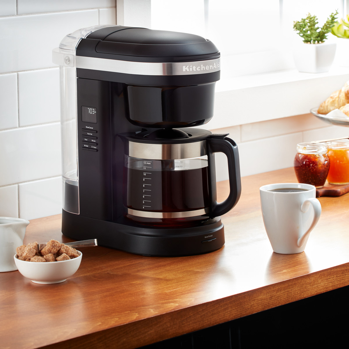 Eine schwarze Kaffeemaschine mit einer Glaskaraffe, eine Tasse Kaffee und Zuckerwürfel auf einer Holztheke.