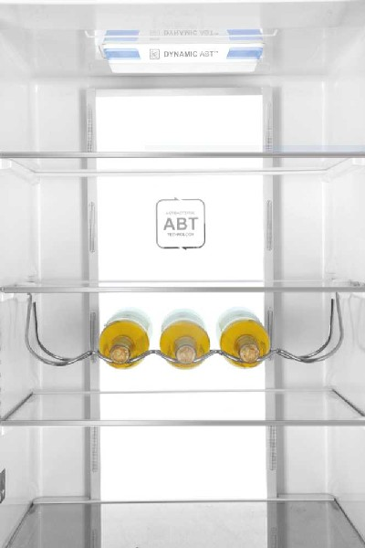 Dentro de un refrigerador con estantes. Tres botellas de vino en un estante metálico.