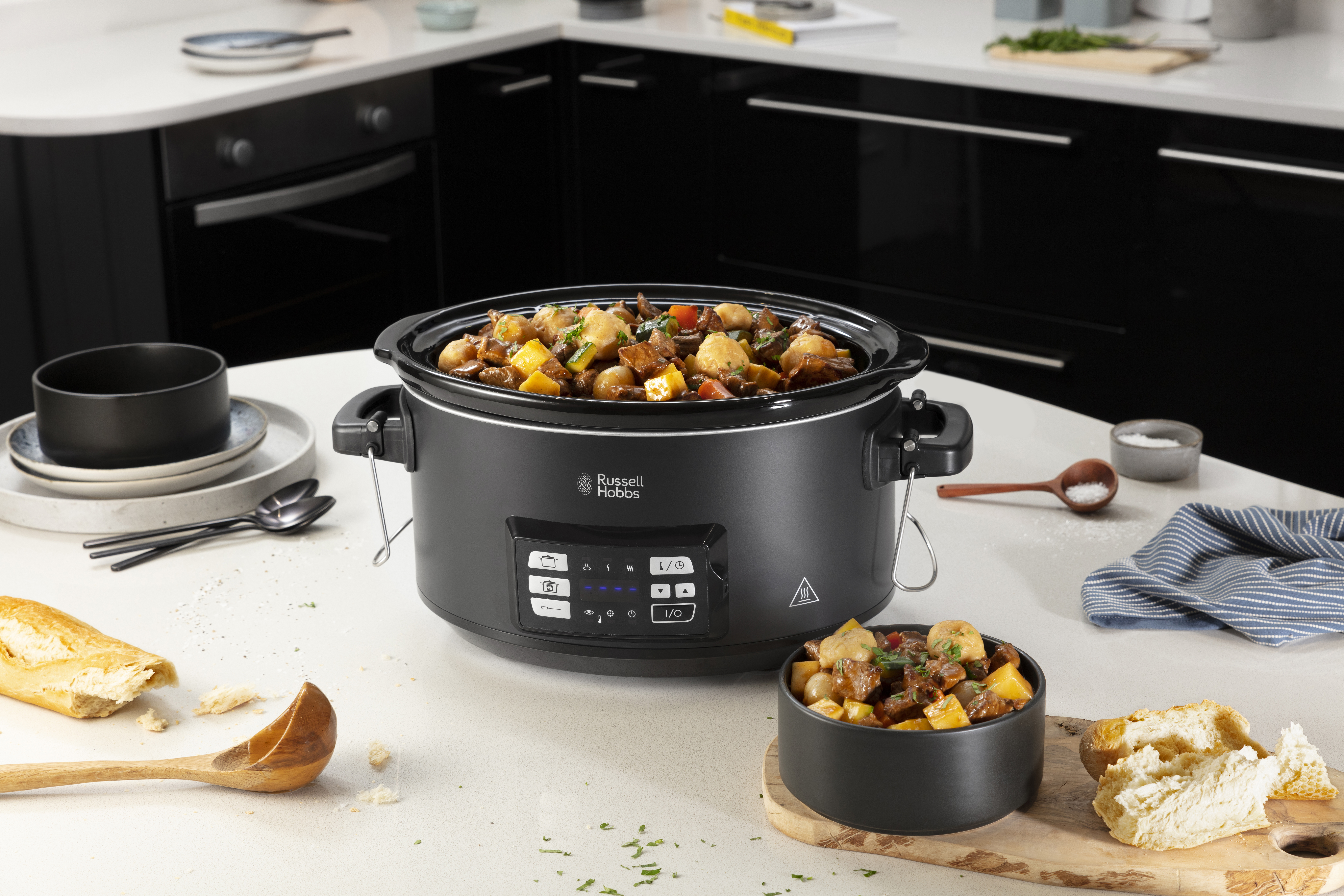 Egy lassú főzőedény pörkölttel, egy tál pörkölt és kenyér a konyhapulton. Russell Hobbs márka.
