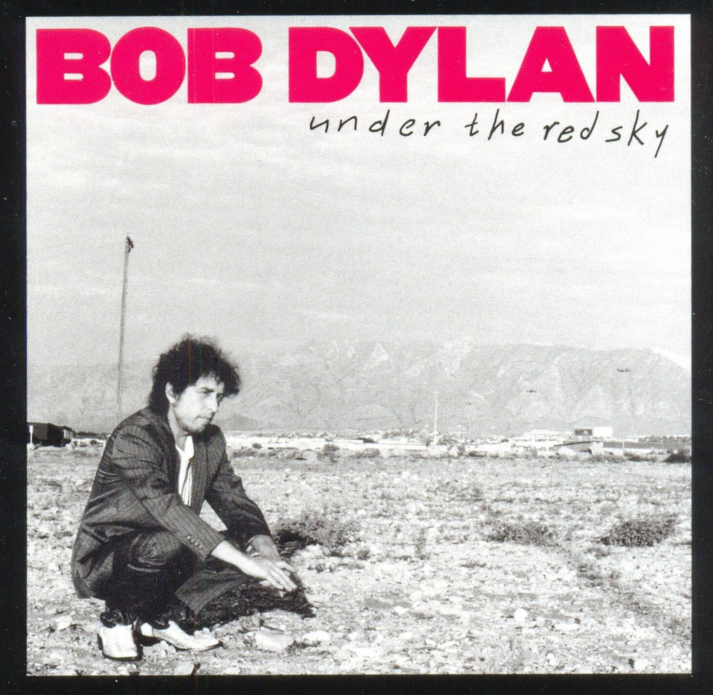 Bob Dylan album borítója, mezőn guggolva, a 'Under the Red Sky' szöveggel.