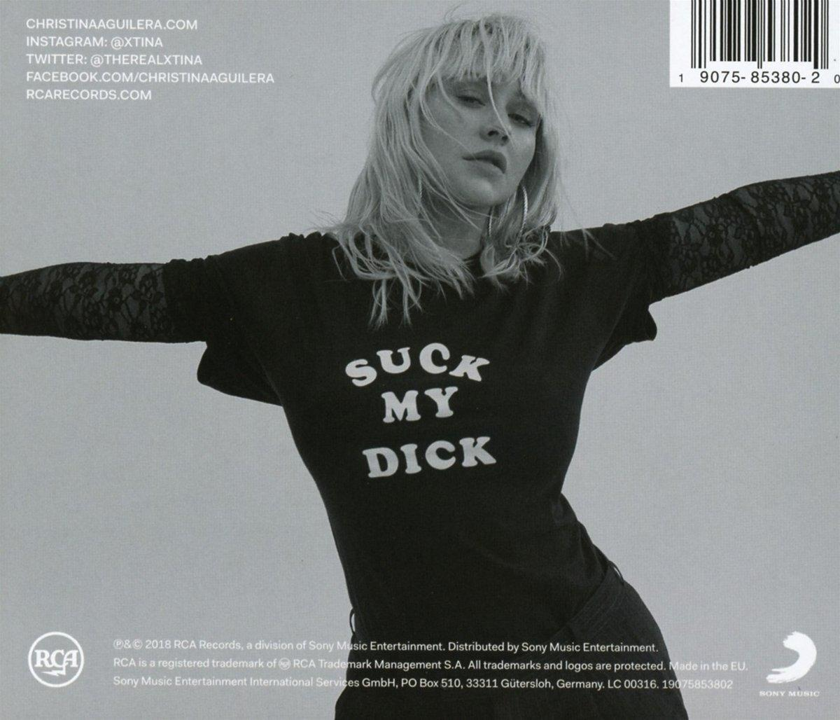 Christina Aguilera fekete pólóban, 'Suck My Dick' felirattal. Kinyújtott karok, szőke haj, vonalkód.