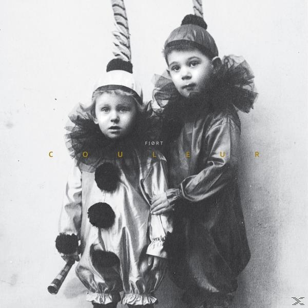 Schwarz-Weiß-Foto von zwei Kindern in Clownkostümen, die eine Requisite halten. Das Wort 'COULEUR' ist sichtbar.