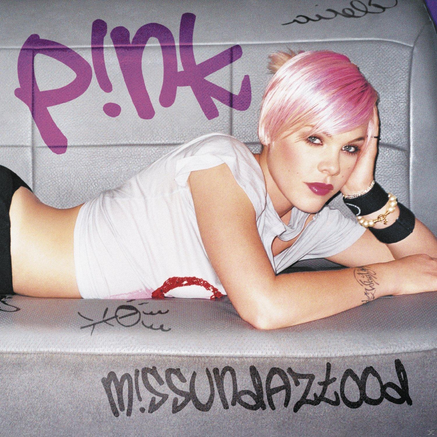 Albumcover von Pink, die auf einer grauen Oberfläche liegt, ein weißes Hemd trägt und rosa Haare hat.