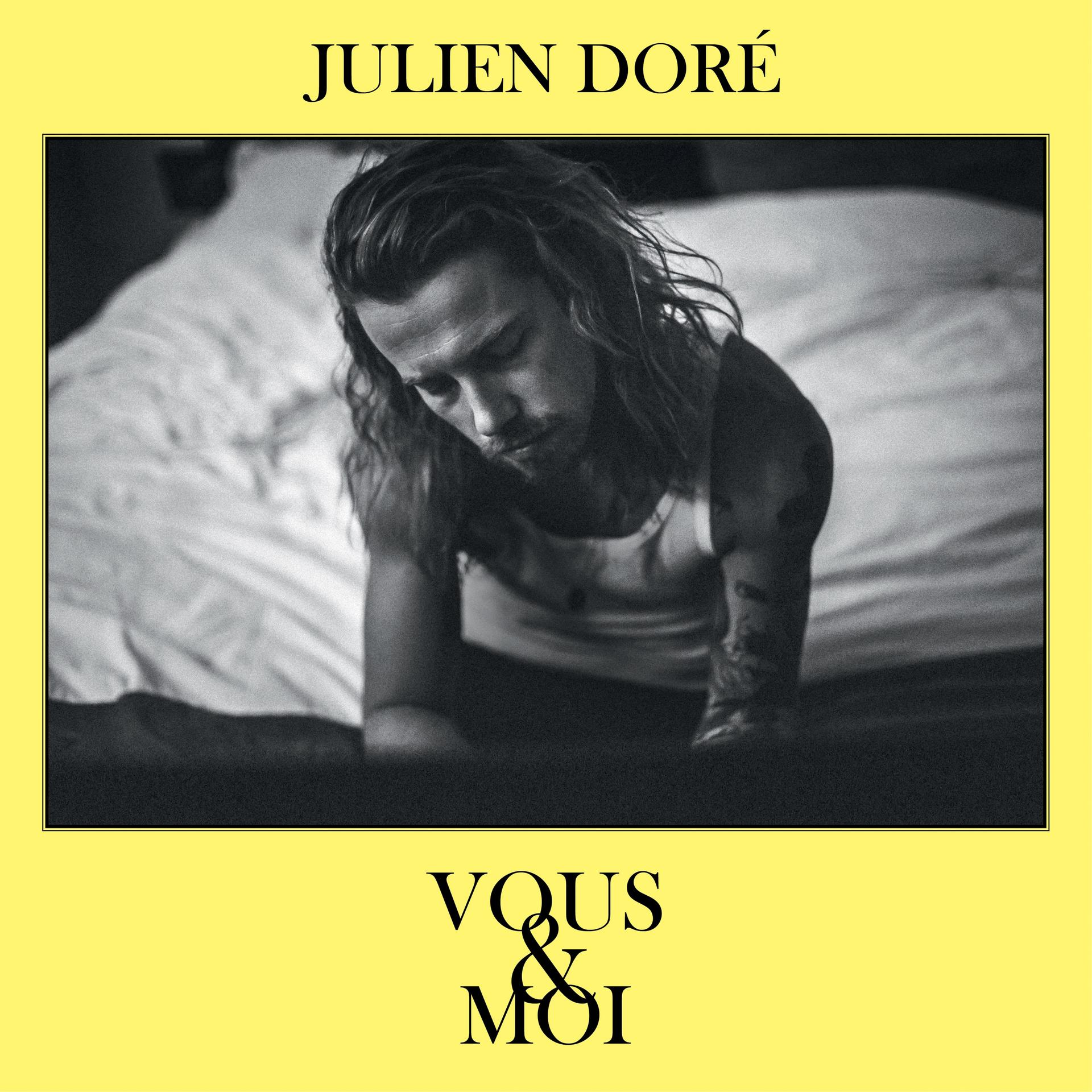 Julien Doré Albumcover. Schwarz-Weiß-Foto eines Mannes auf einem Bett, gelber Rand.