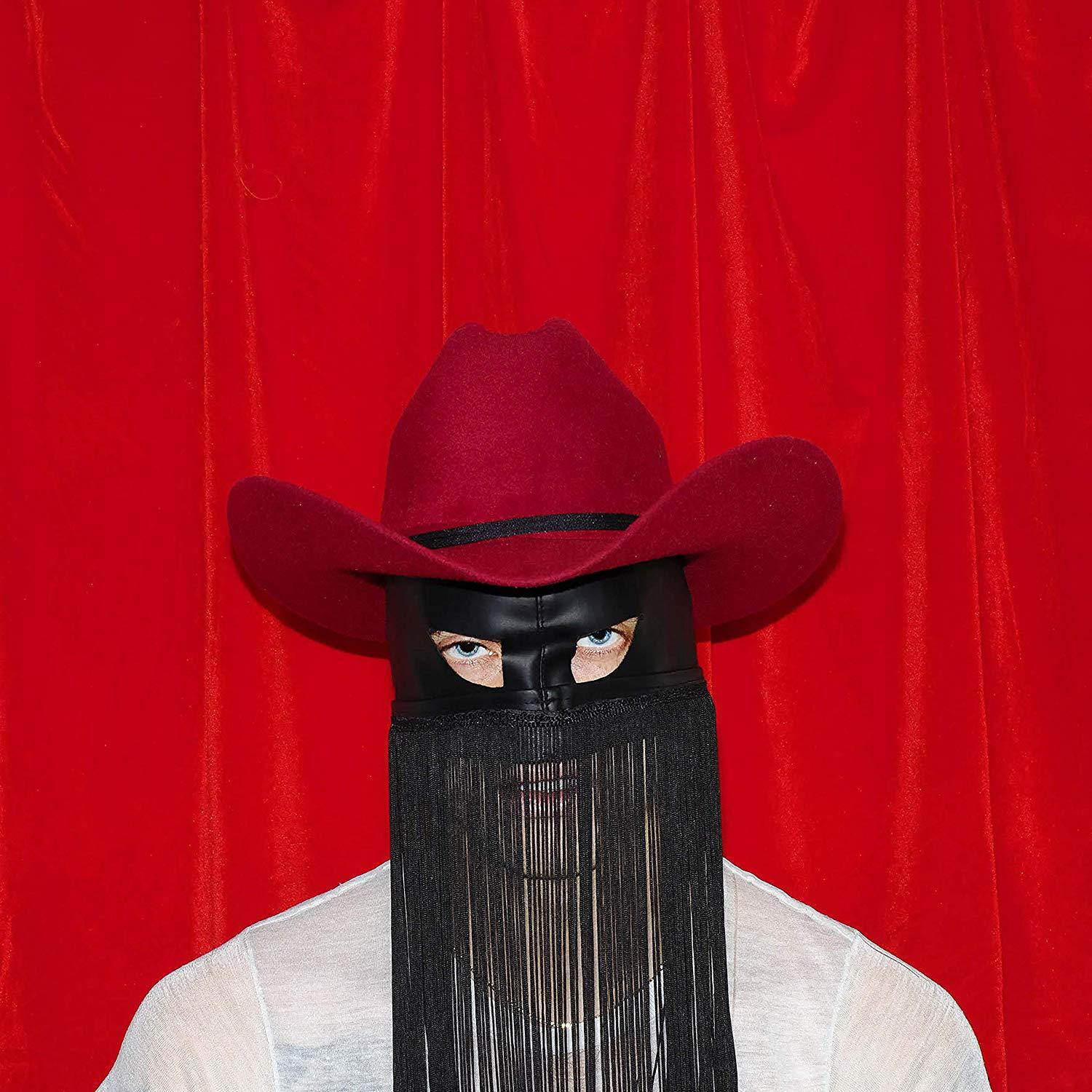 Person trägt roten Cowboyhut, schwarze Maske mit Fransen, roter Hintergrund.