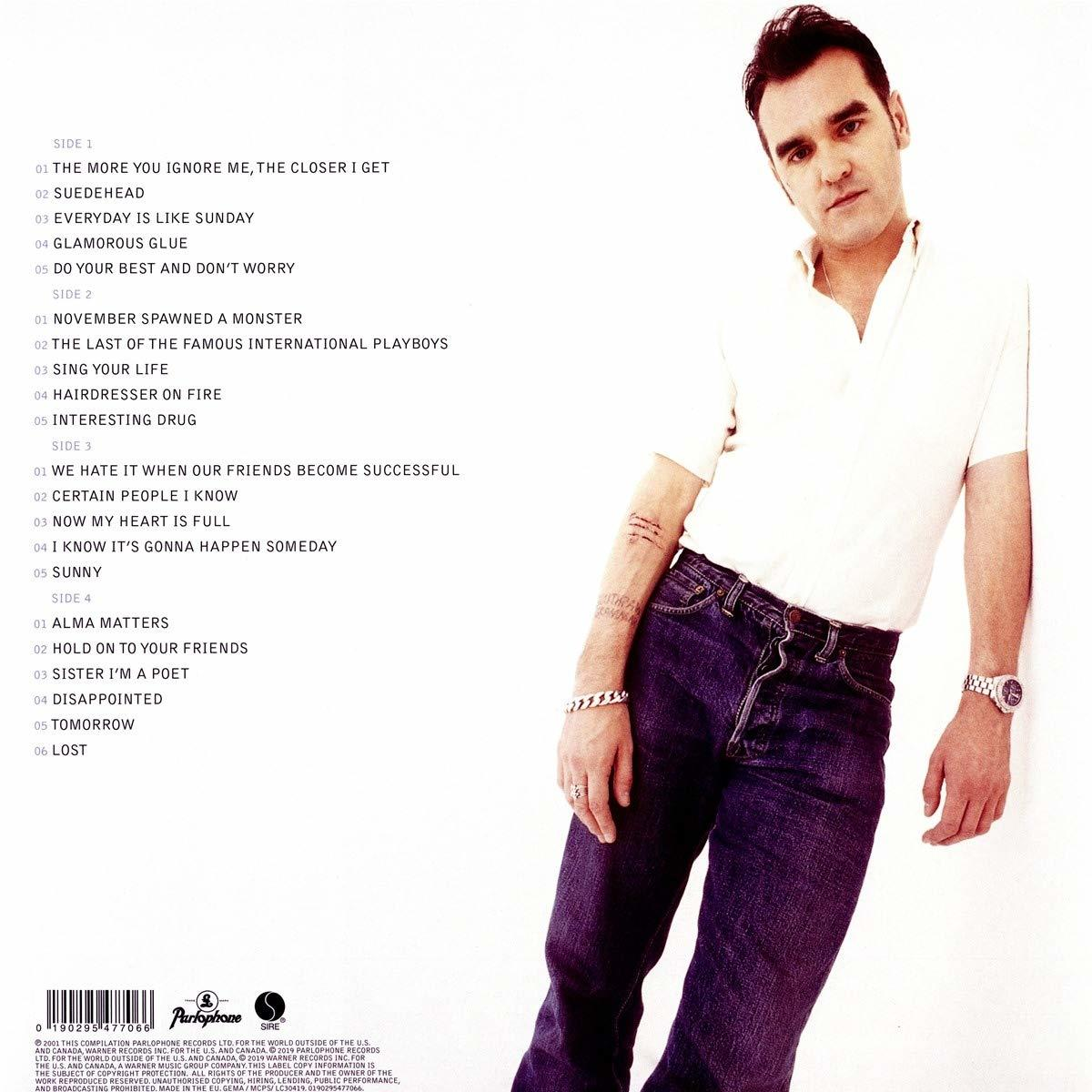 Ein Mann in einem weißen Hemd und Jeans, der sich an eine Wand lehnt.