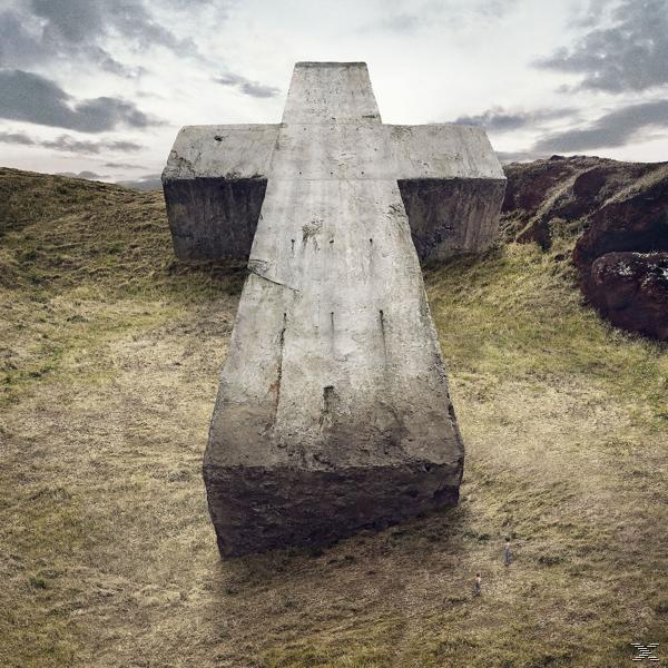Justice albumhoes. Een groot betonnen kruis staat op een grasheuvel onder een bewolkte hemel.