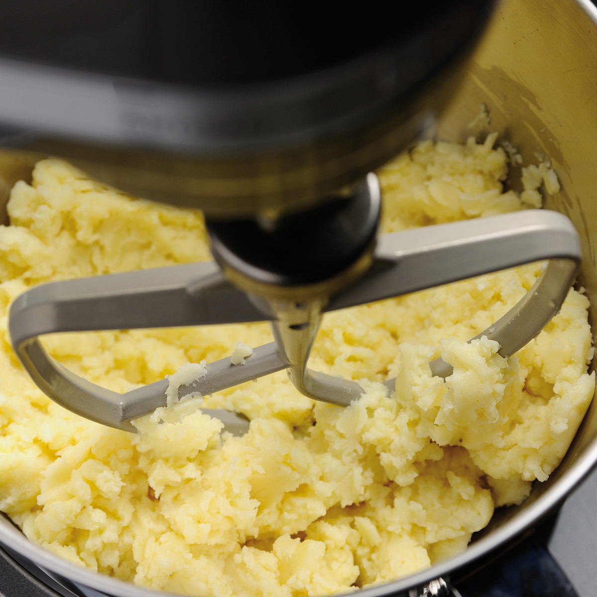 Mixer in einer Metallschüssel, der gelbes Kartoffelpüree verrührt. Nahaufnahme.