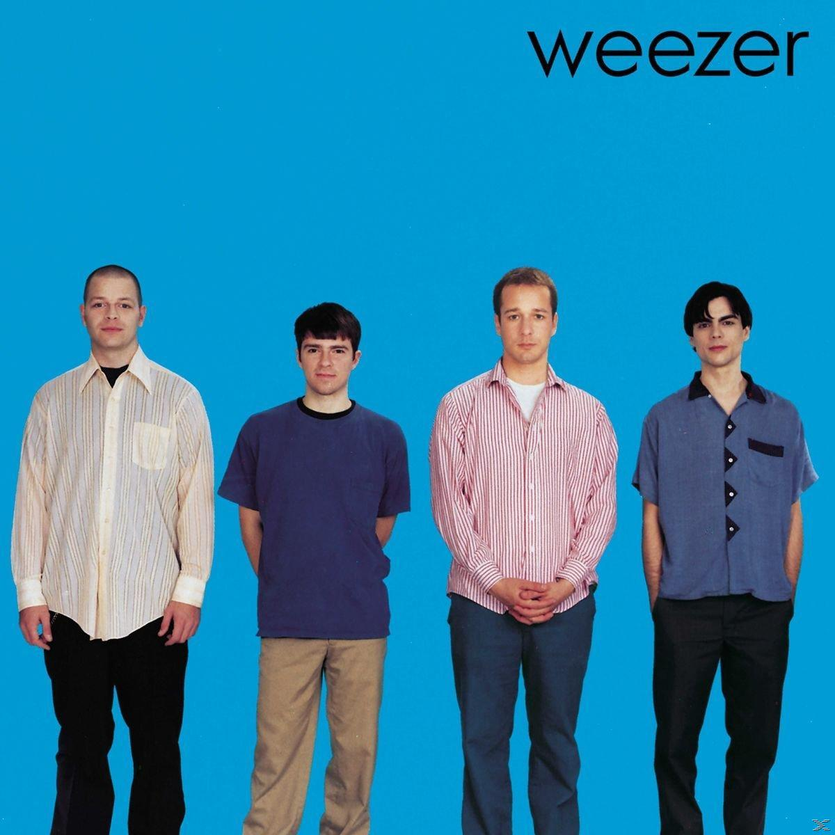 Vier Männer stehen vor einem blauen Hintergrund. Der Schriftzug 'weezer' steht oben.