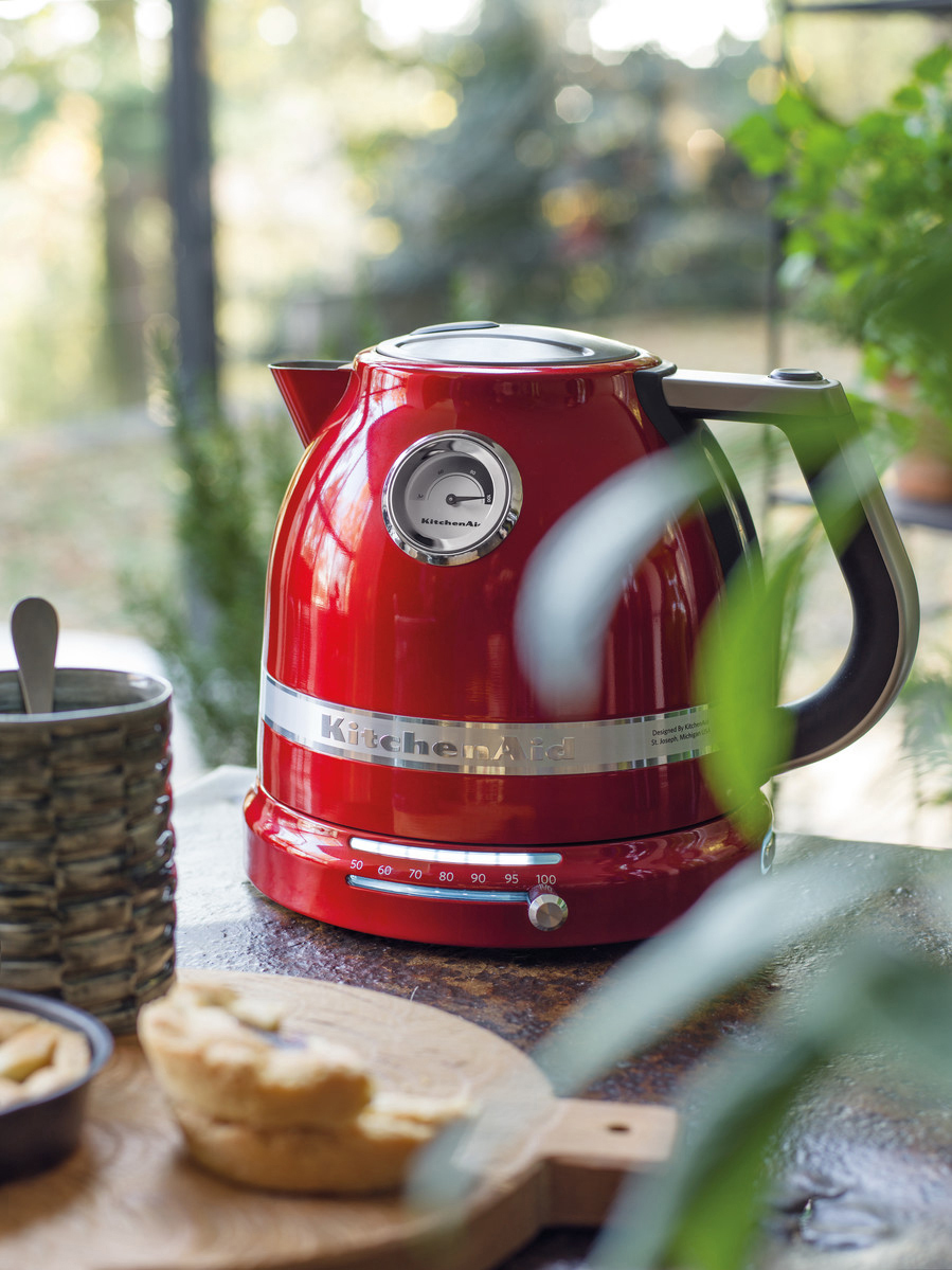 Ein roter Wasserkocher mit Temperaturanzeige und ein Holzbrett mit Speisen.
