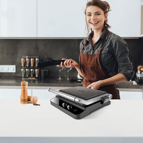 Una mujer sonriente en una cocina con una parrilla y utensilios de cocina en una encimera blanca.