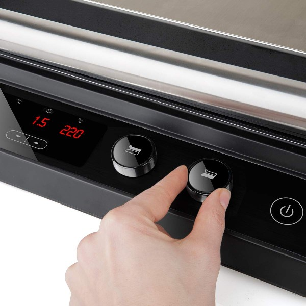 Una mano gira la perilla de una parrilla eléctrica negra con una pantalla digital que muestra 220.