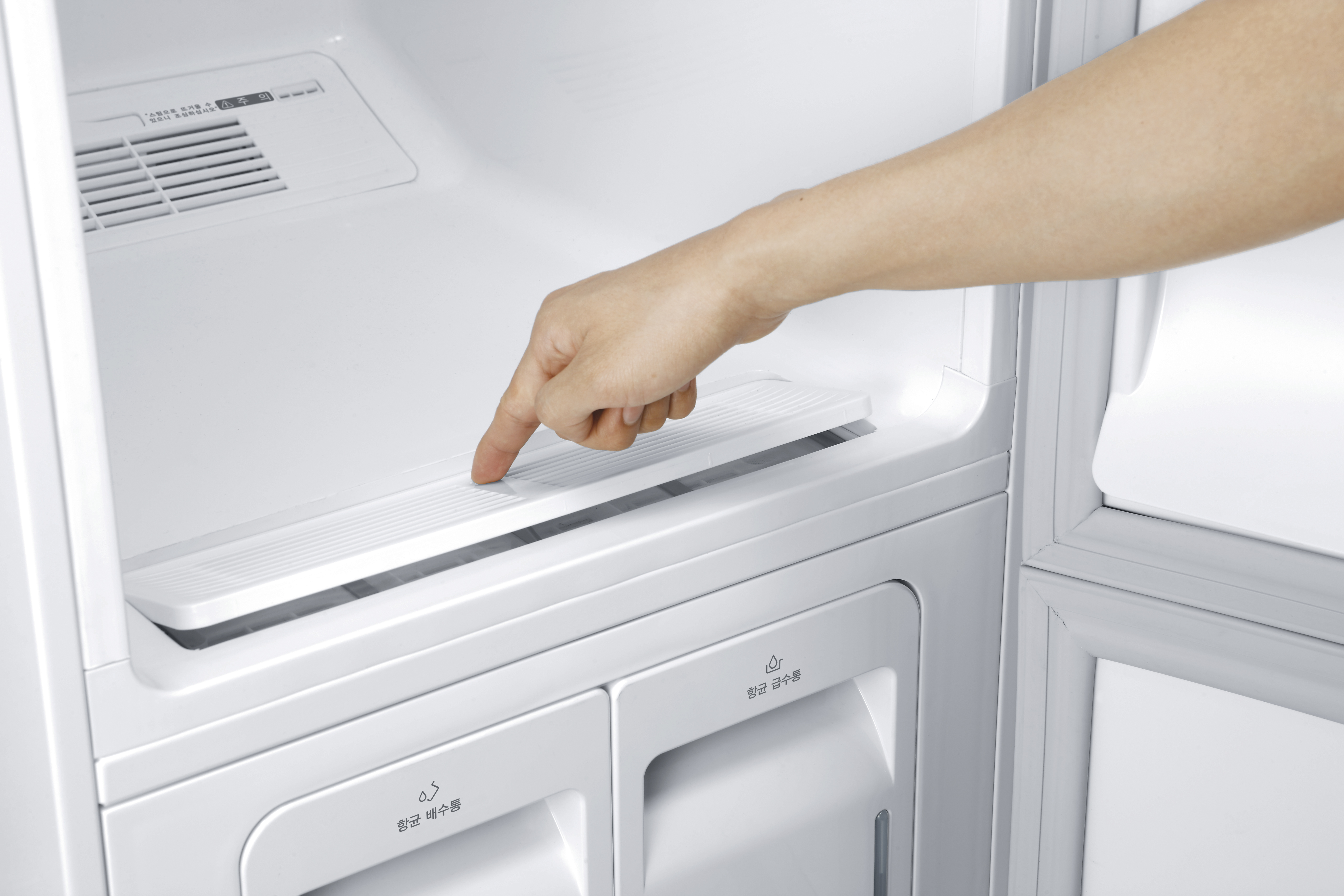 Die Hand einer Person greift in einen weißen Kühlschrank, um auf ein Regal zuzugreifen.