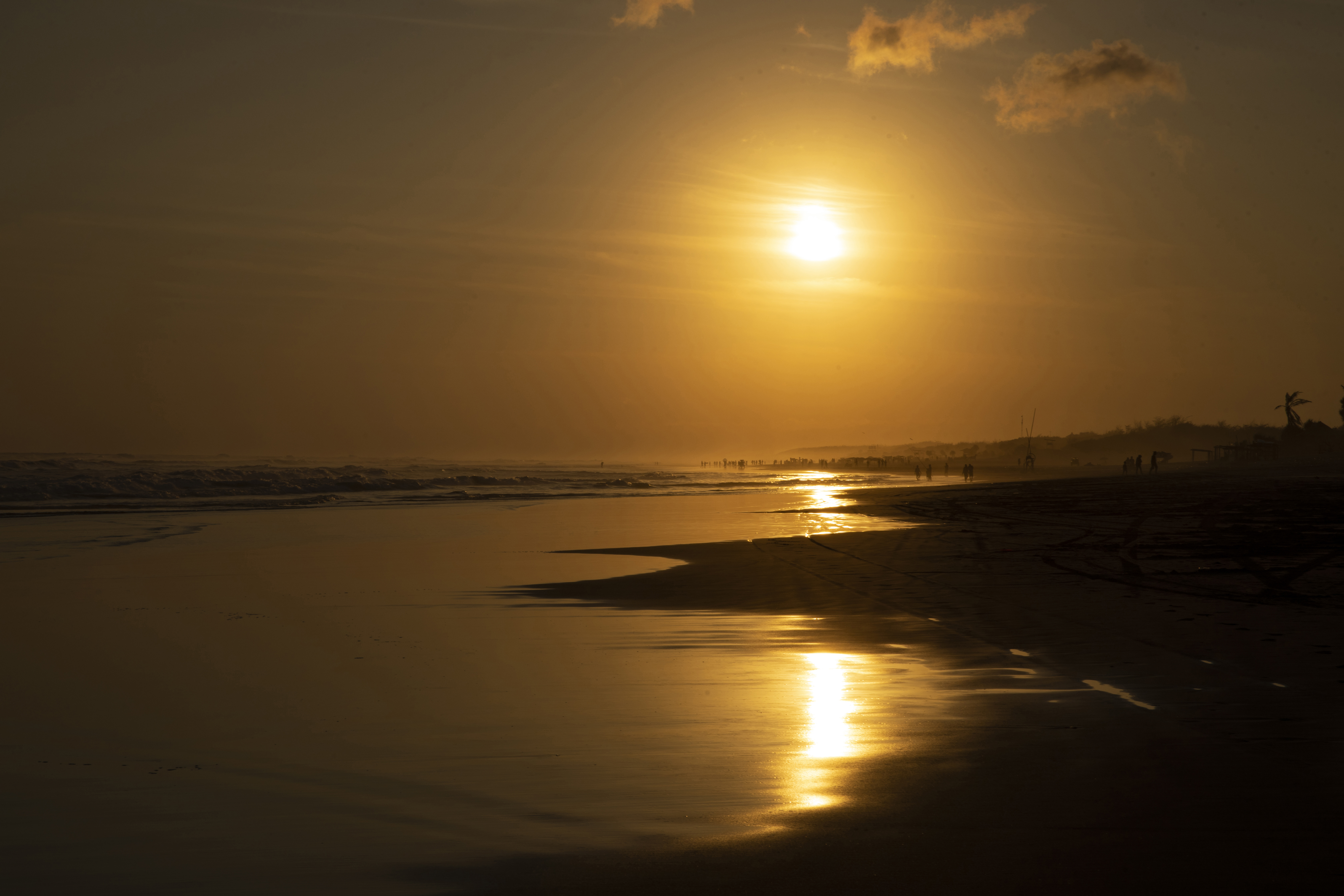 Sonnenuntergang über einem Strand mit goldenen Reflexen im nassen Sand.