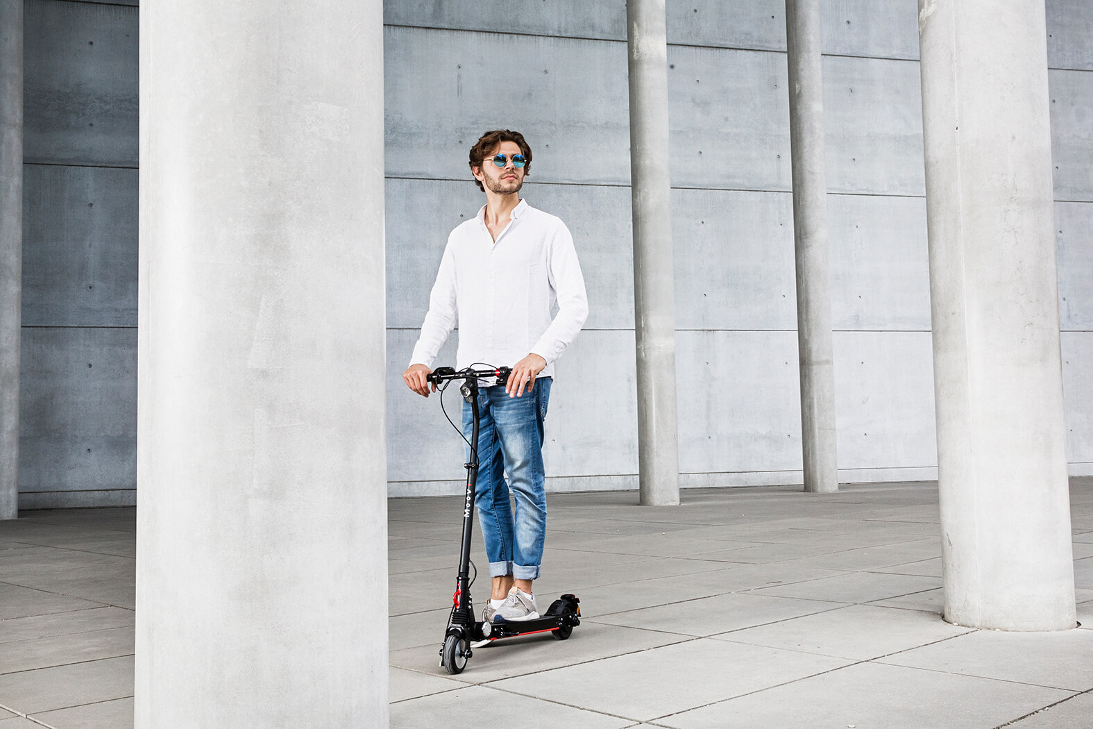 Ein Mann mit Sonnenbrille auf einem schwarzen Roller steht zwischen Betonpfeilern.