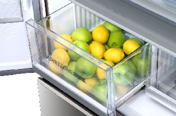 Un cajón de refrigerador con limones y manzanas verdes. El cajón es transparente, la fruta visible.