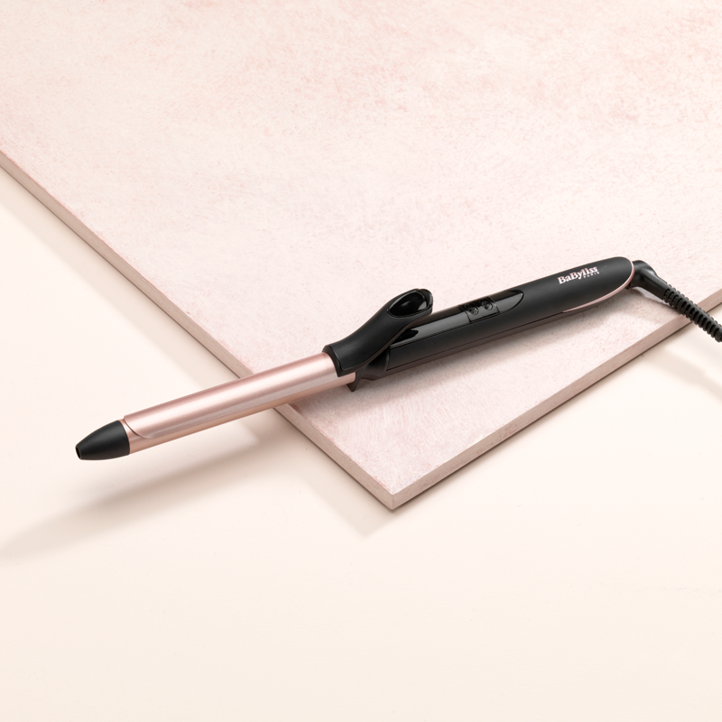 Un fer à friser noir et or rose est présenté sur une surface rose.