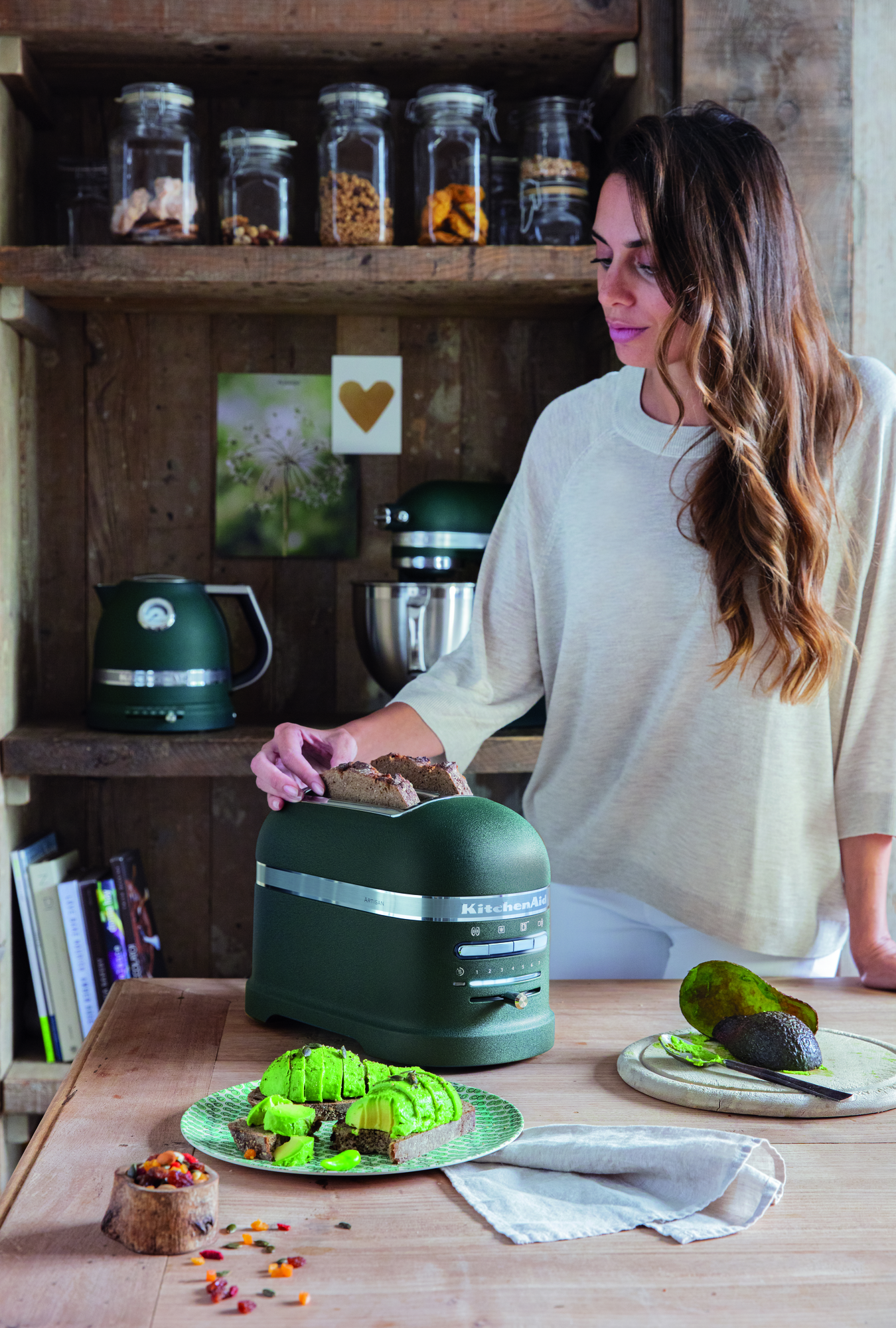 Frau mit Toast und Avocado mit grünem KitchenAid-Toaster und passendem Wasserkocher.