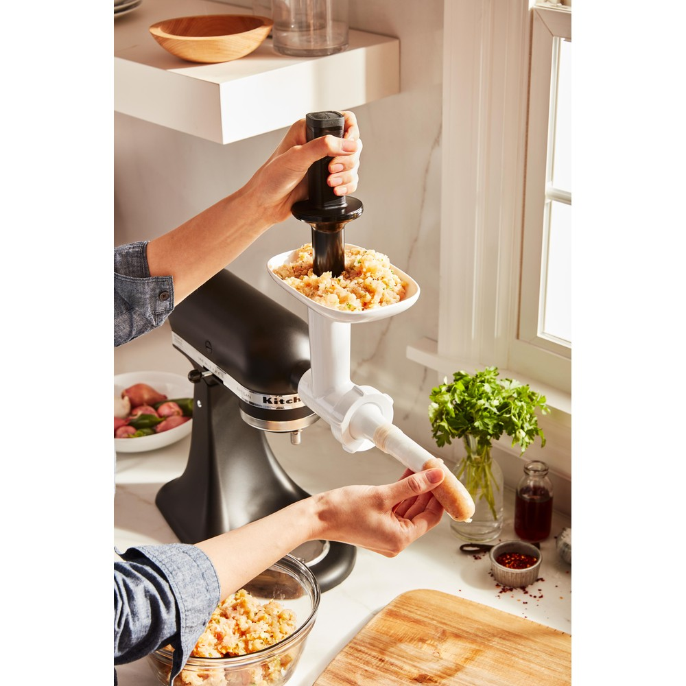 Hände benutzen einen KitchenAid-Aufsatz zum Zerkleinern von Fleisch, mit Fleisch und Zutaten.