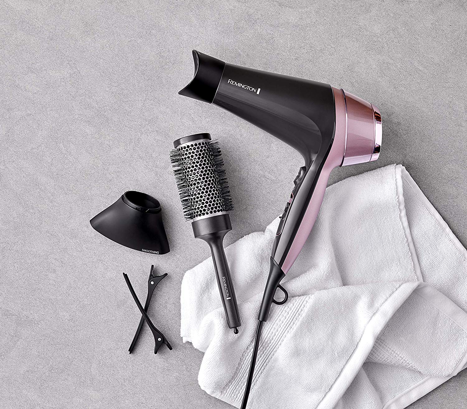 Hair dryer with a brush and accessories on a grey surface with a white towel.