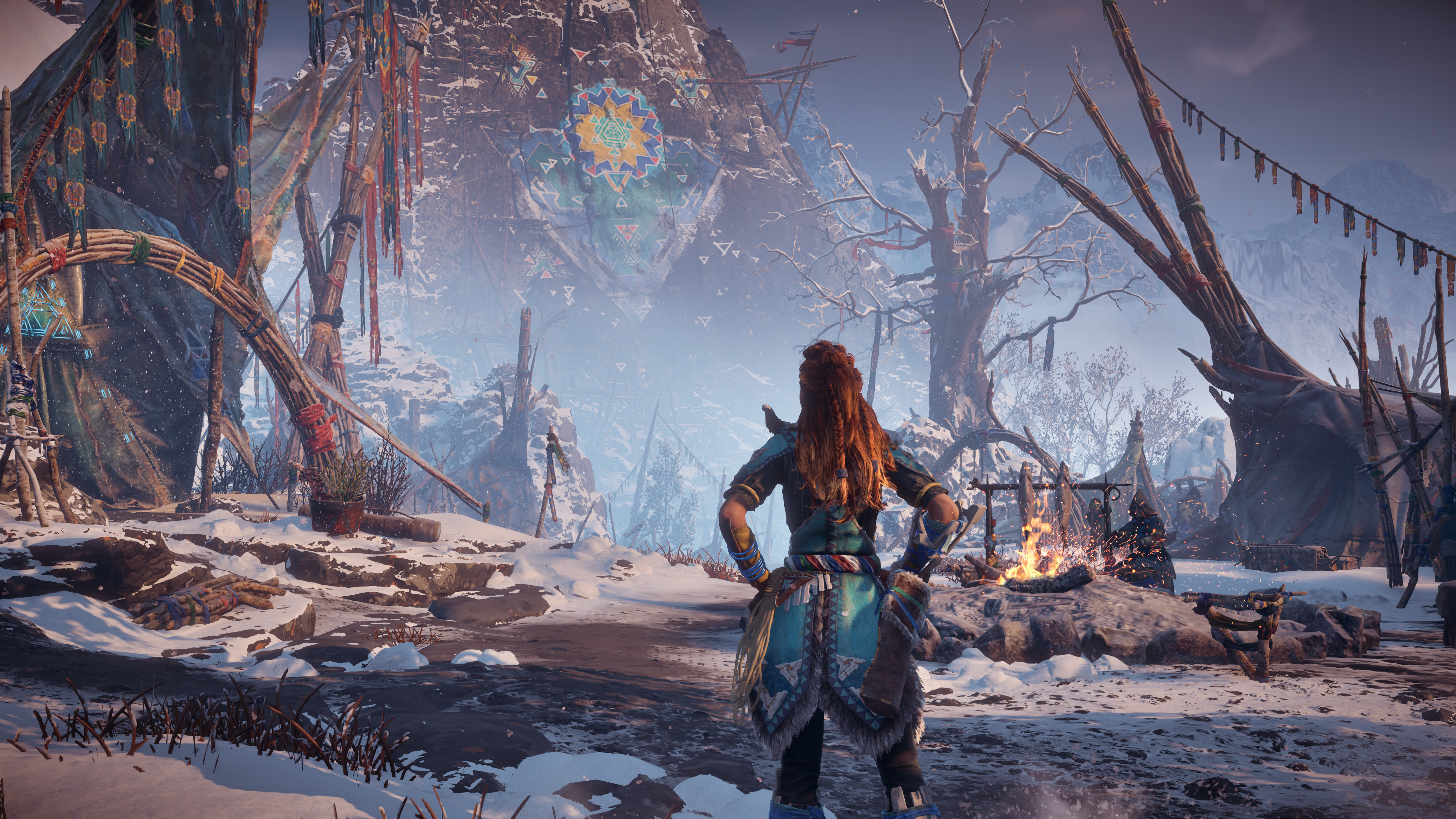 Frau in verschneiter Berglandschaft aus 'Horizon Zero Dawn'. Sie blickt auf Struktur.