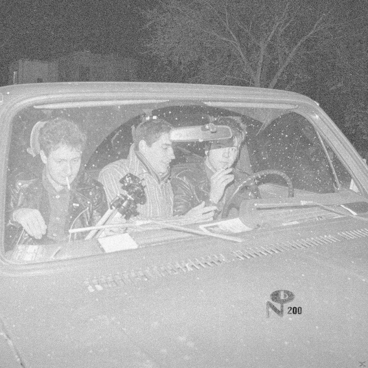 Schwarz-Weiß-Foto von drei Personen in einem Auto. Einer raucht, die anderen schauen nach vorne.