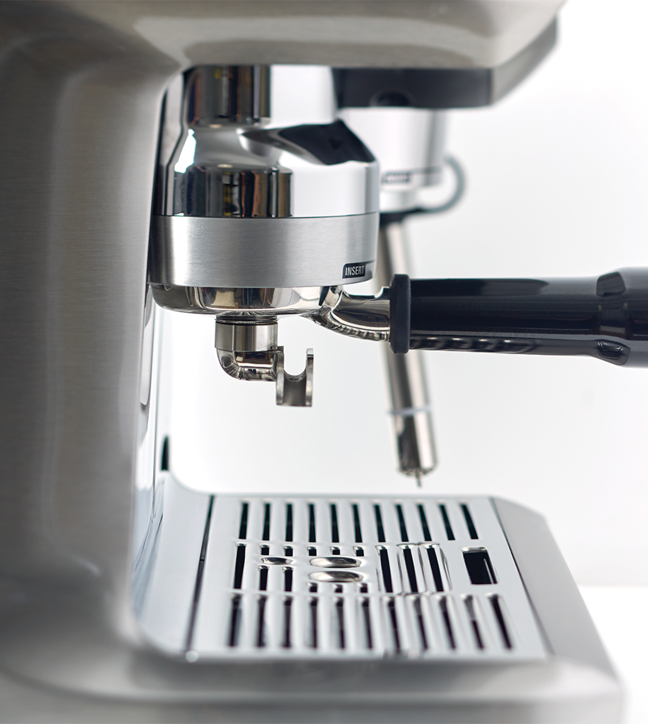 Close-up van een zilverkleurige espressomachine. Een portafilter is geplaatst. Een lekbakje staat eronder.