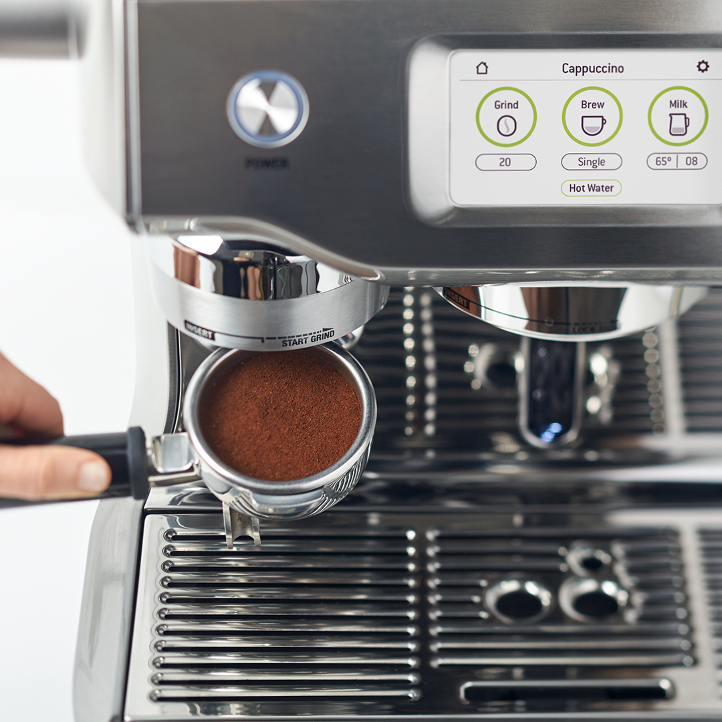 Close-up van een zilveren espressomachine. Een hand houdt de portafilter vast.