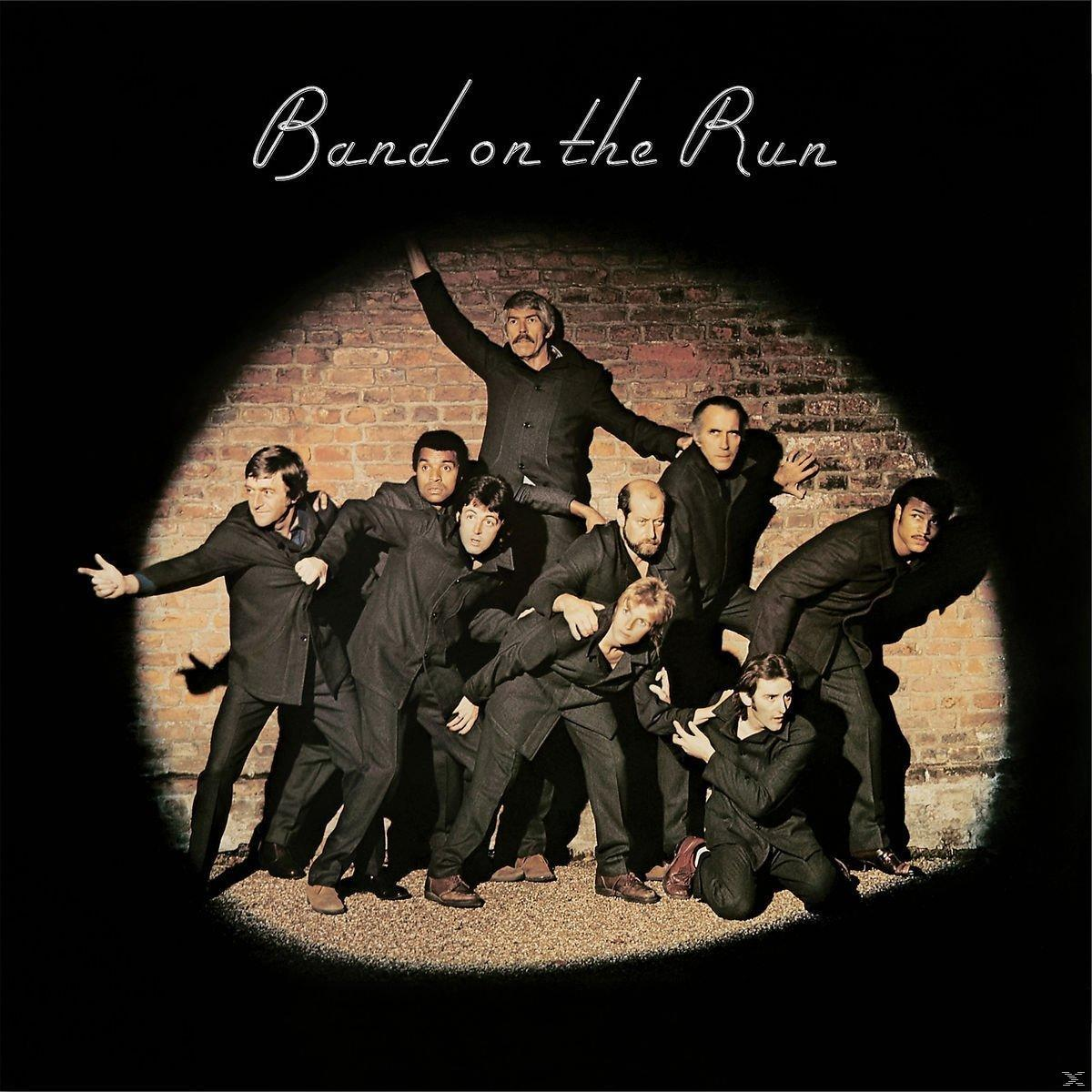 Albumcover mit neun Männern in schwarzen Anzügen vor einer Backsteinmauer unter einem Scheinwerfer.