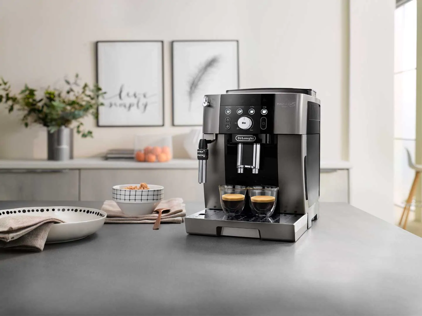 Une machine à expresso argentée et noire avec deux tasses à café sur un comptoir gris.