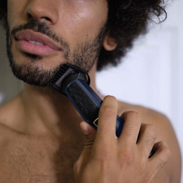 Un hombre recortando su barba con una recortadora eléctrica.