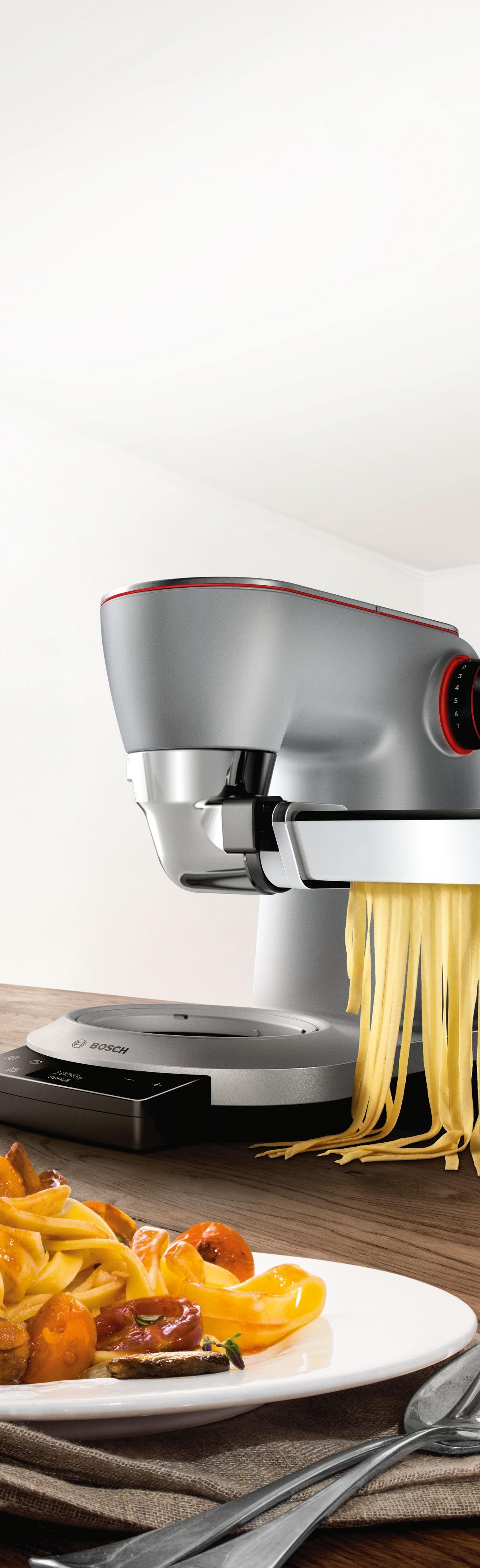 Konyhai robotgép friss tésztát készít, mellette egy tányér tészta szósszal.