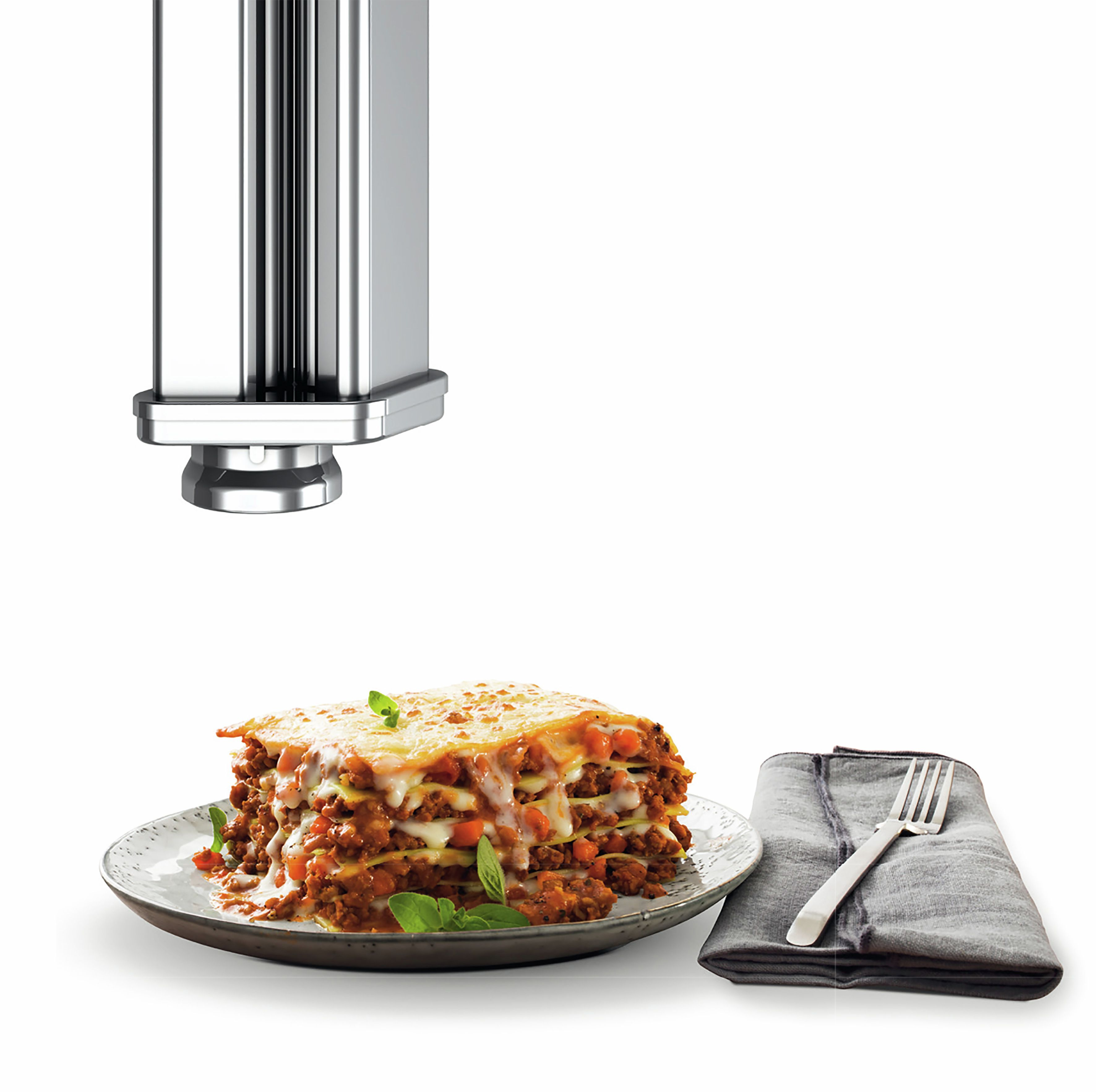 Lasagne húsos szósszal tányéron, mellette evőeszközök anyagon.