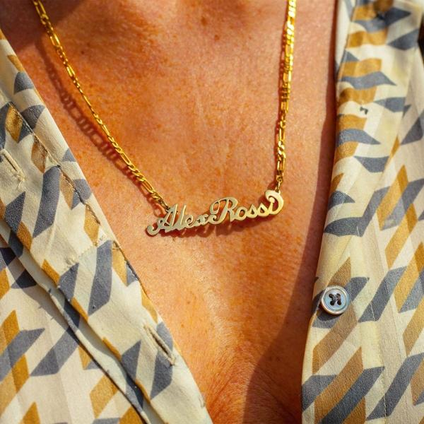 Eine goldene Halskette mit dem Namen 'Alexa Ross' in kursiver Schrift auf der Brust einer Person.