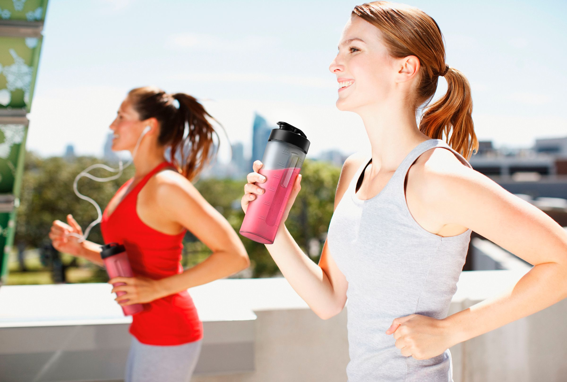 Deux femmes courant avec des shakers de protéines. L'une tient un shake rose, l'autre a des écouteurs.