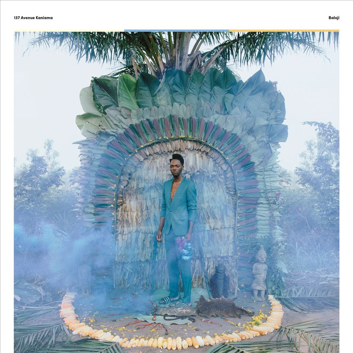 Man in teal pak staat voor een versierde boog. Hij houdt bloemen vast. Kleurrijke decoraties omringen hem.
