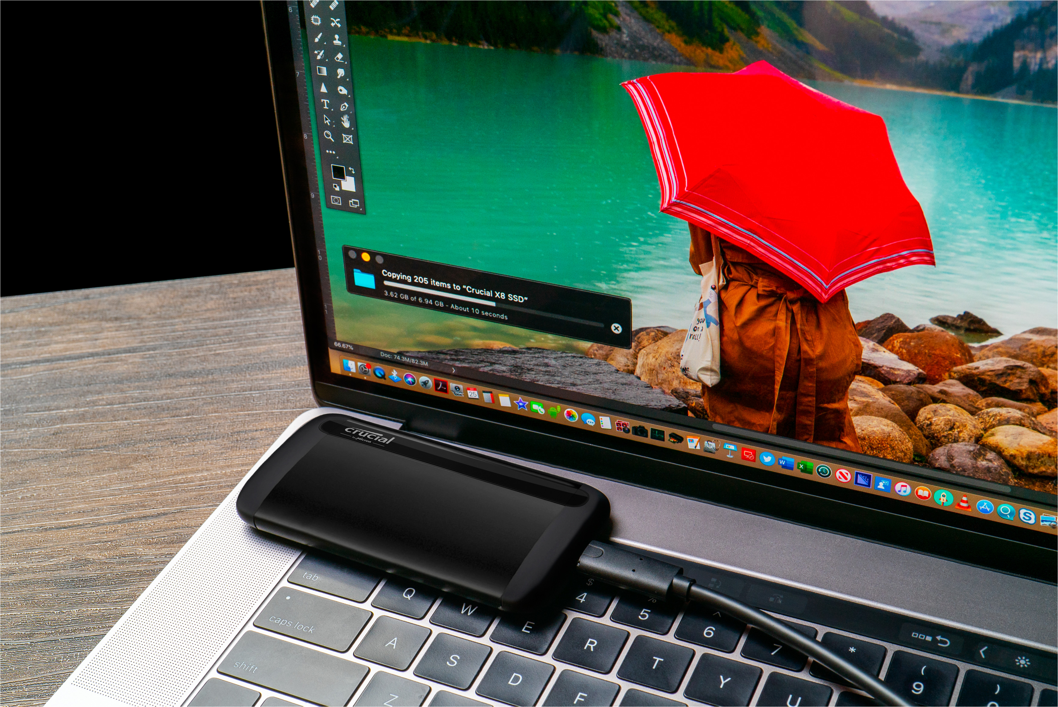 Laptop mit angeschlossener Crucial X8 SSD. Eine Person mit rotem Regenschirm steht am See auf dem Bildschirm.