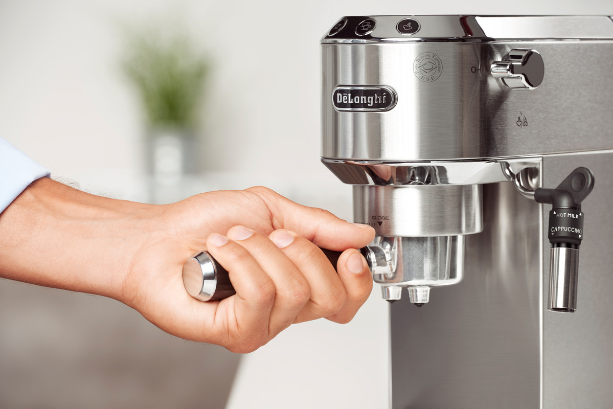 Eine Hand bedient eine Espresso-Maschine von De'Longhi aus Edelstahl. Der Siebträger wird verriegelt.