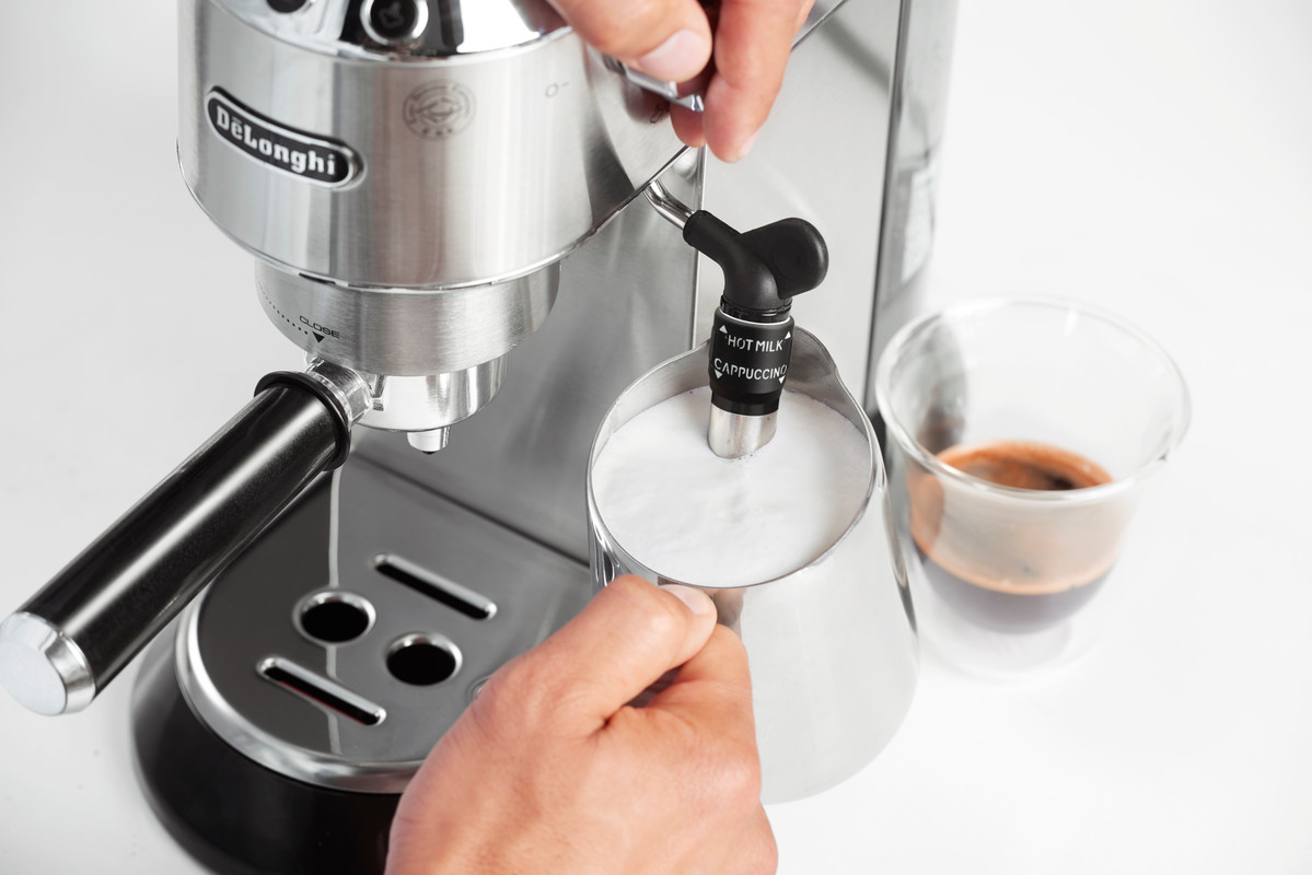 Espressomaschine, die Milch in einem Metallkrug aufschäumt, mit einem Glas Espresso.