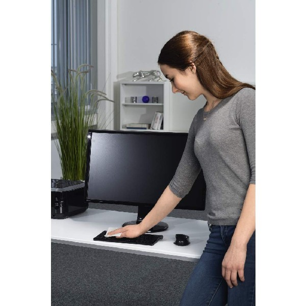 Una mujer limpiando un teclado de computadora en un escritorio blanco.