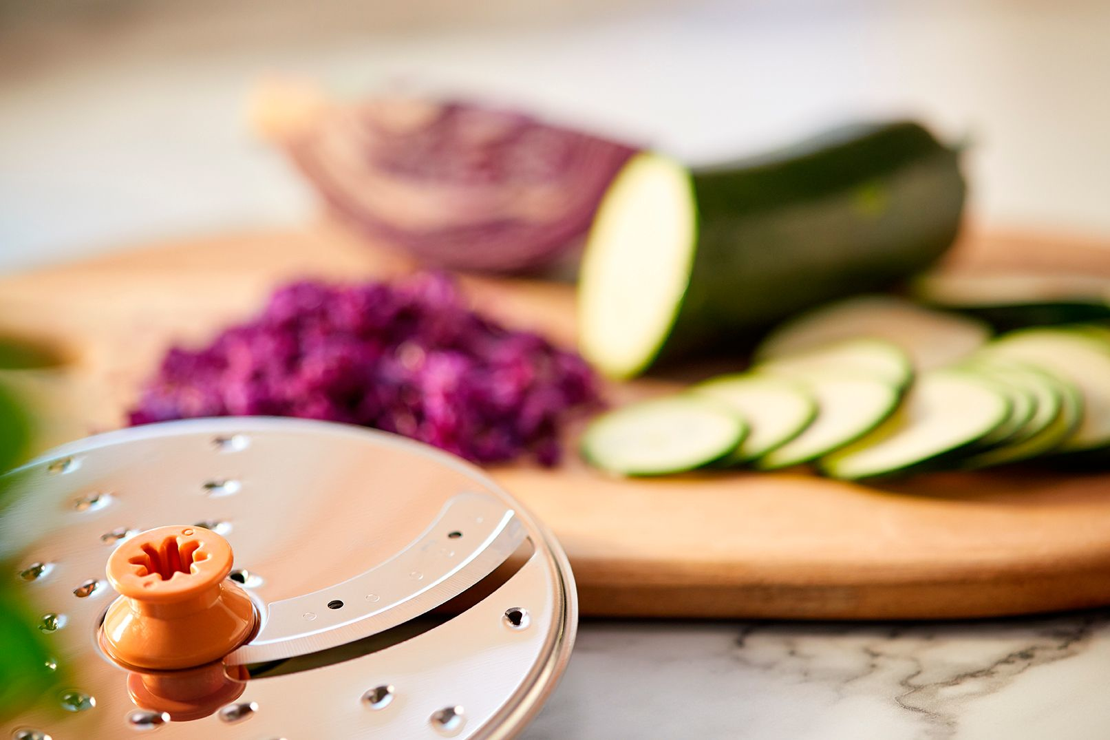 Gemüse und ein Schneider auf einem Holzbrett. Zucchini und Rotkohl sind sichtbar.