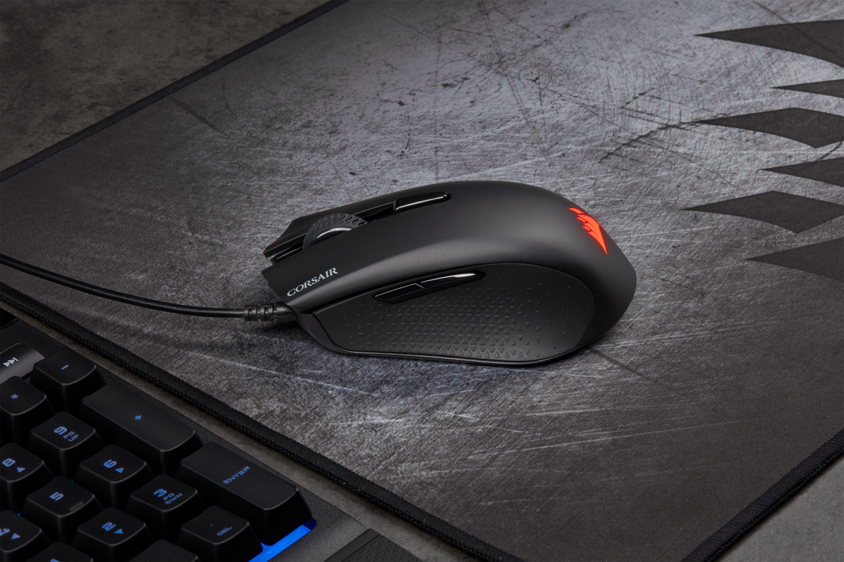 Souris de jeu noire sur un tapis de souris gris, avec un clavier partiellement en arrière-plan.