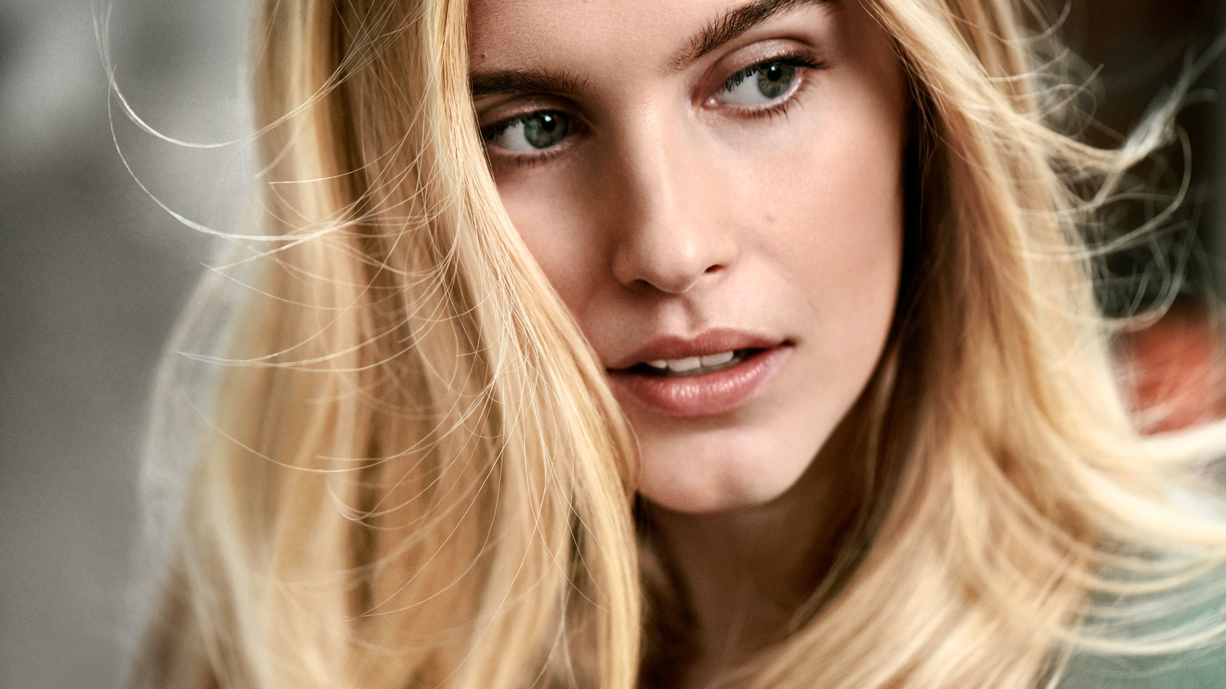Blonde Frau mit langem Haar, die wegschaut. Das Haar weht im Wind.