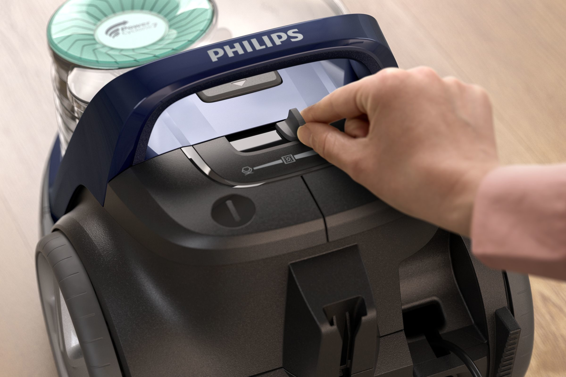 Una mano aziona un pulsante su un aspirapolvere Philips. L'aspirapolvere è blu, con una parte superiore trasparente.