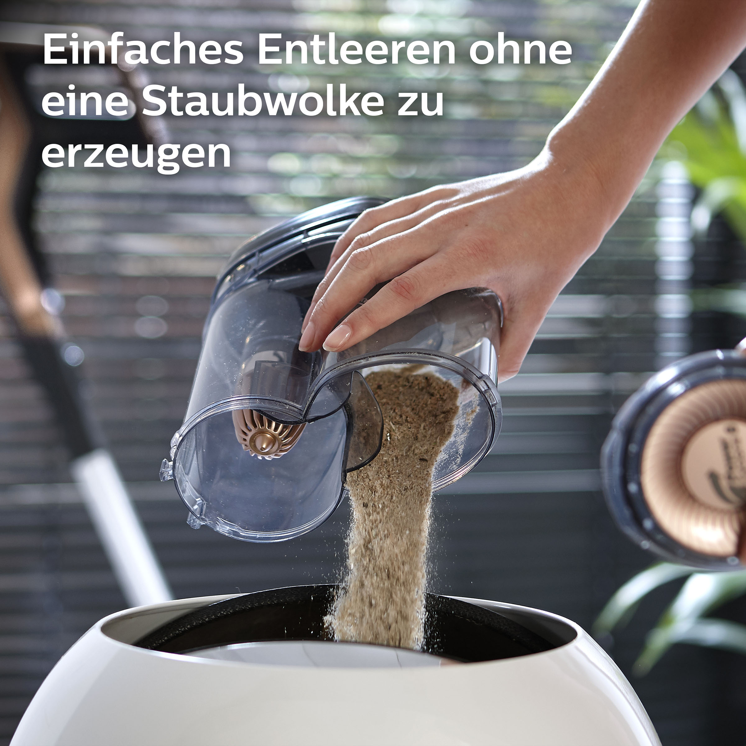 Eine Hand entleert einen Staubsaugerbehälter in einen weißen Behälter.